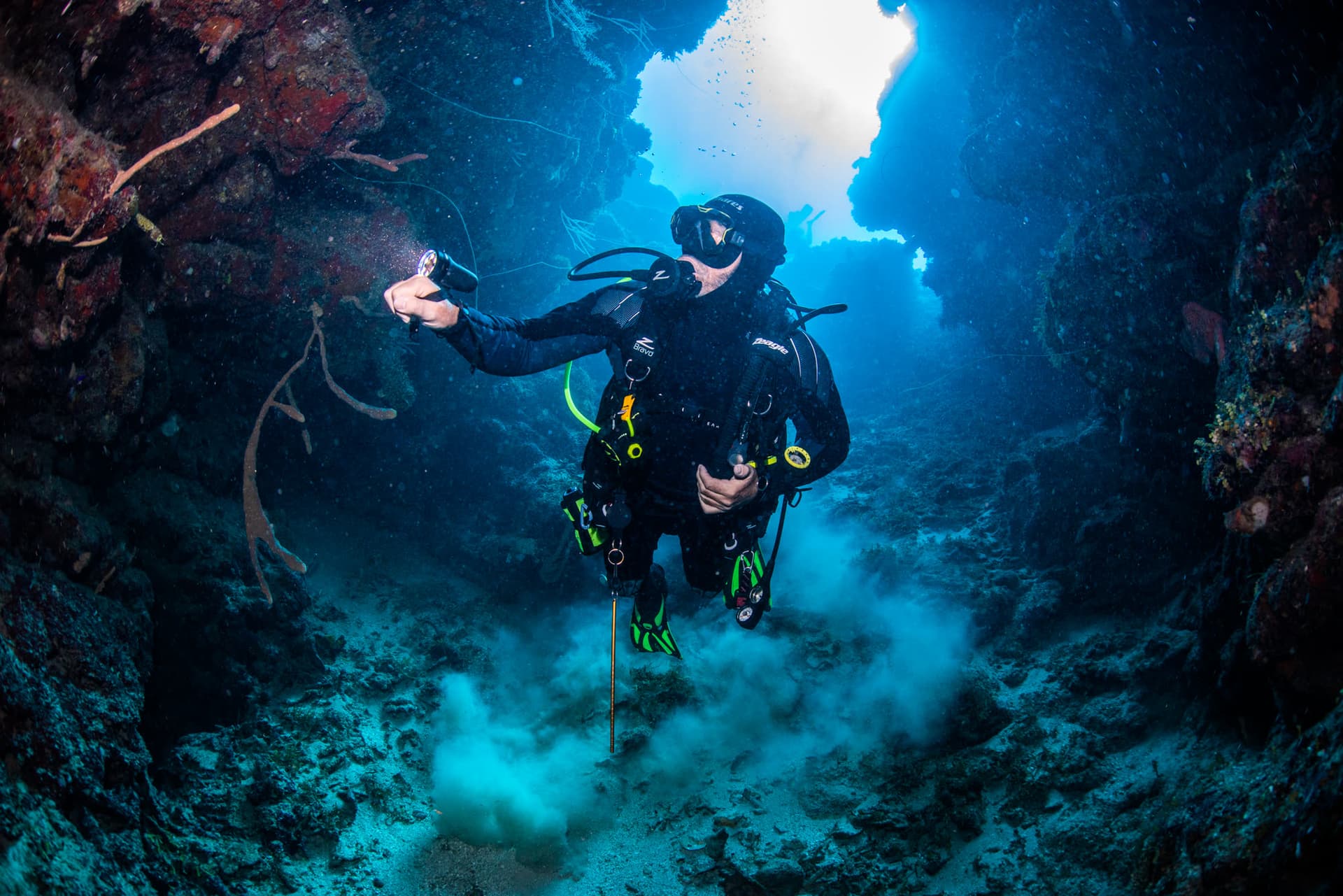 A diver rising out of a reef swim-through into open water, Roatan
